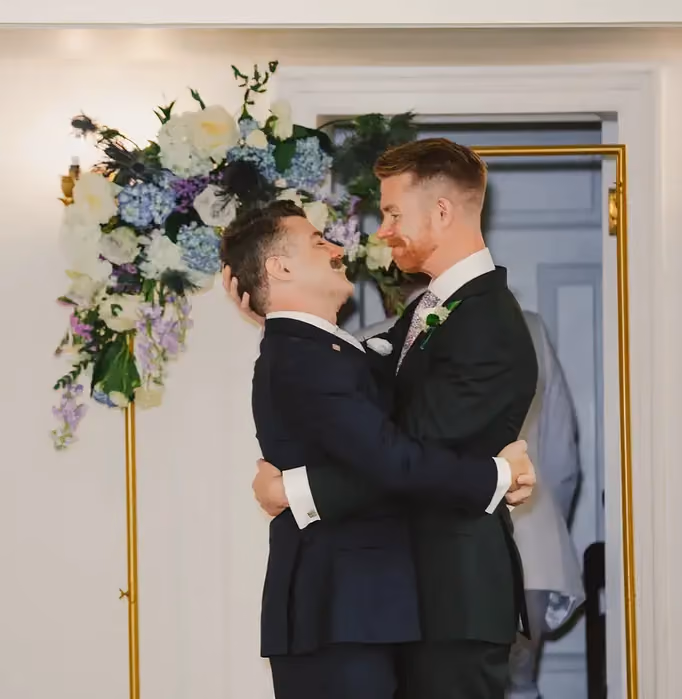 Grooms standing before a Twilight-toned floral arch backdrop