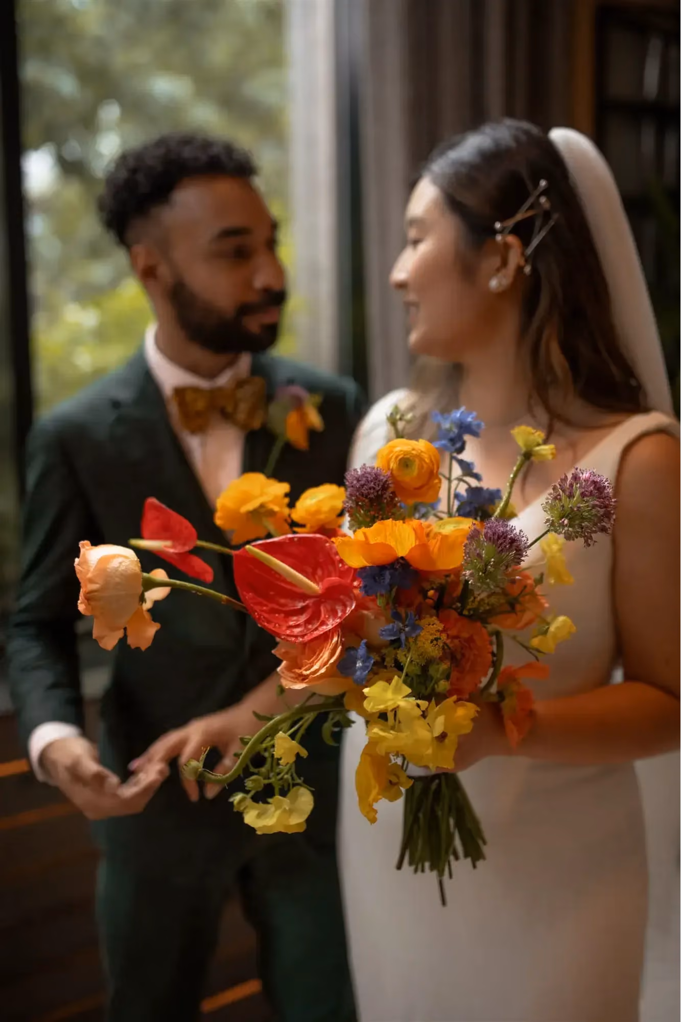 Bride holding colorful Ikebana-inspired bouquet with red anthurium, yellow ranunculus, and blue flowers.