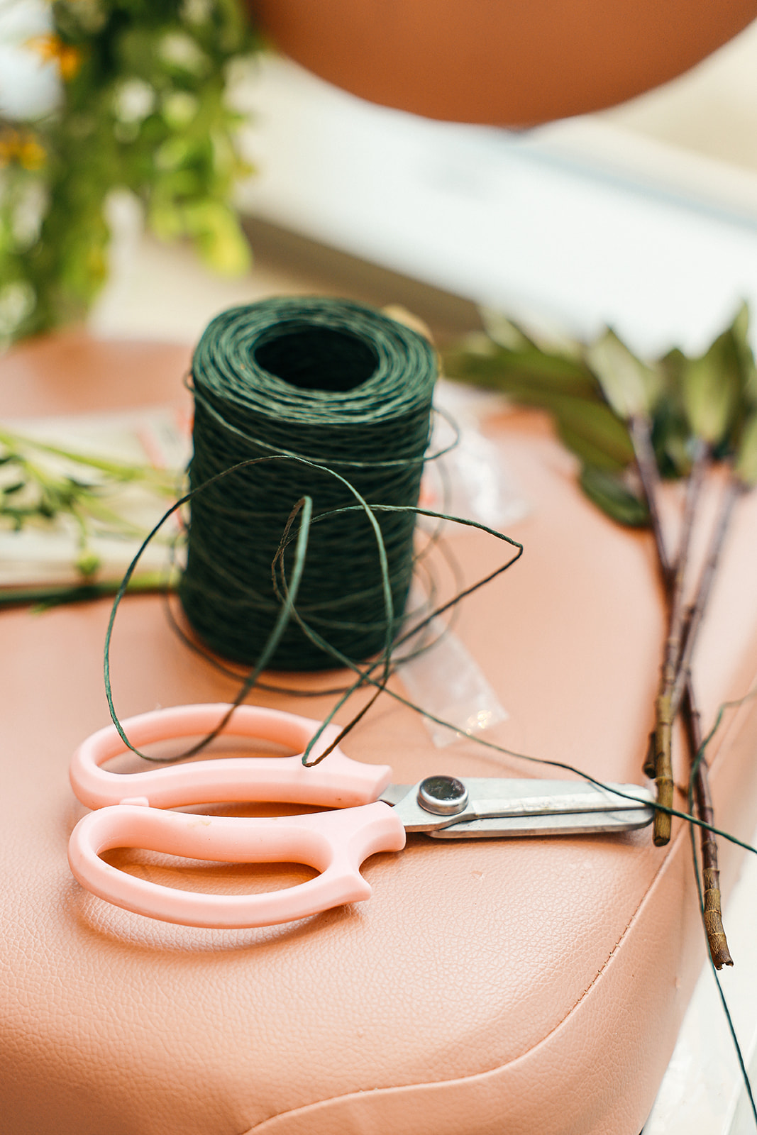 Close-up of florist tools including green floral wire, pink-handled shears, and stems on a work surface