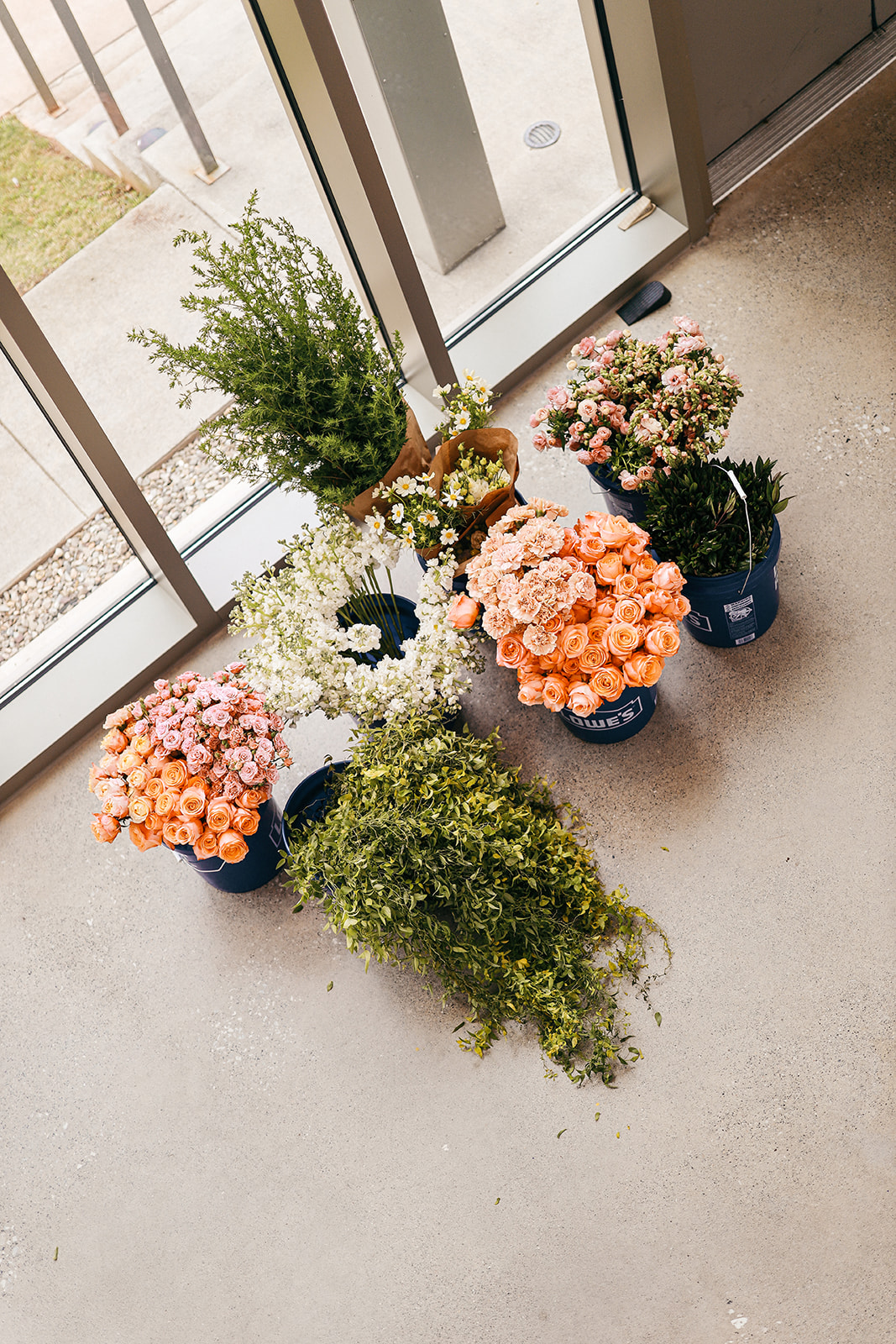 Overhead view of fresh flower buckets with peach garden roses, white blooms, and greenery ready for processing near a doorway