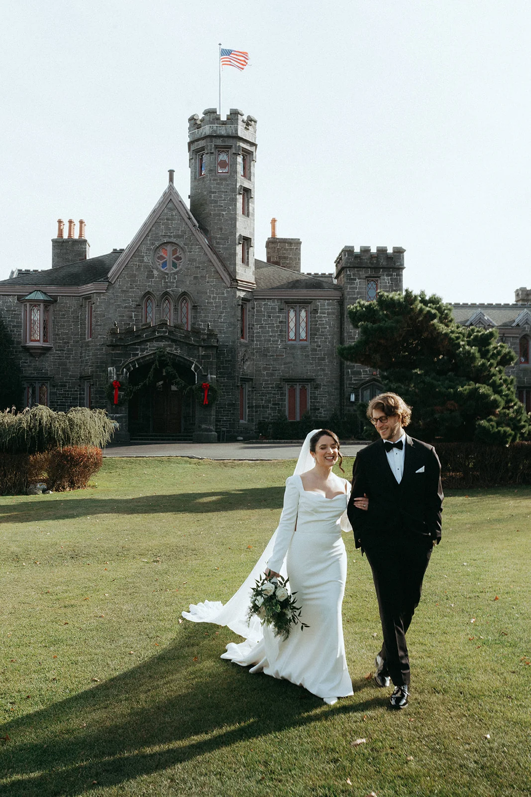 Bride and groom walking across a lawn in front of a castle-like stone building