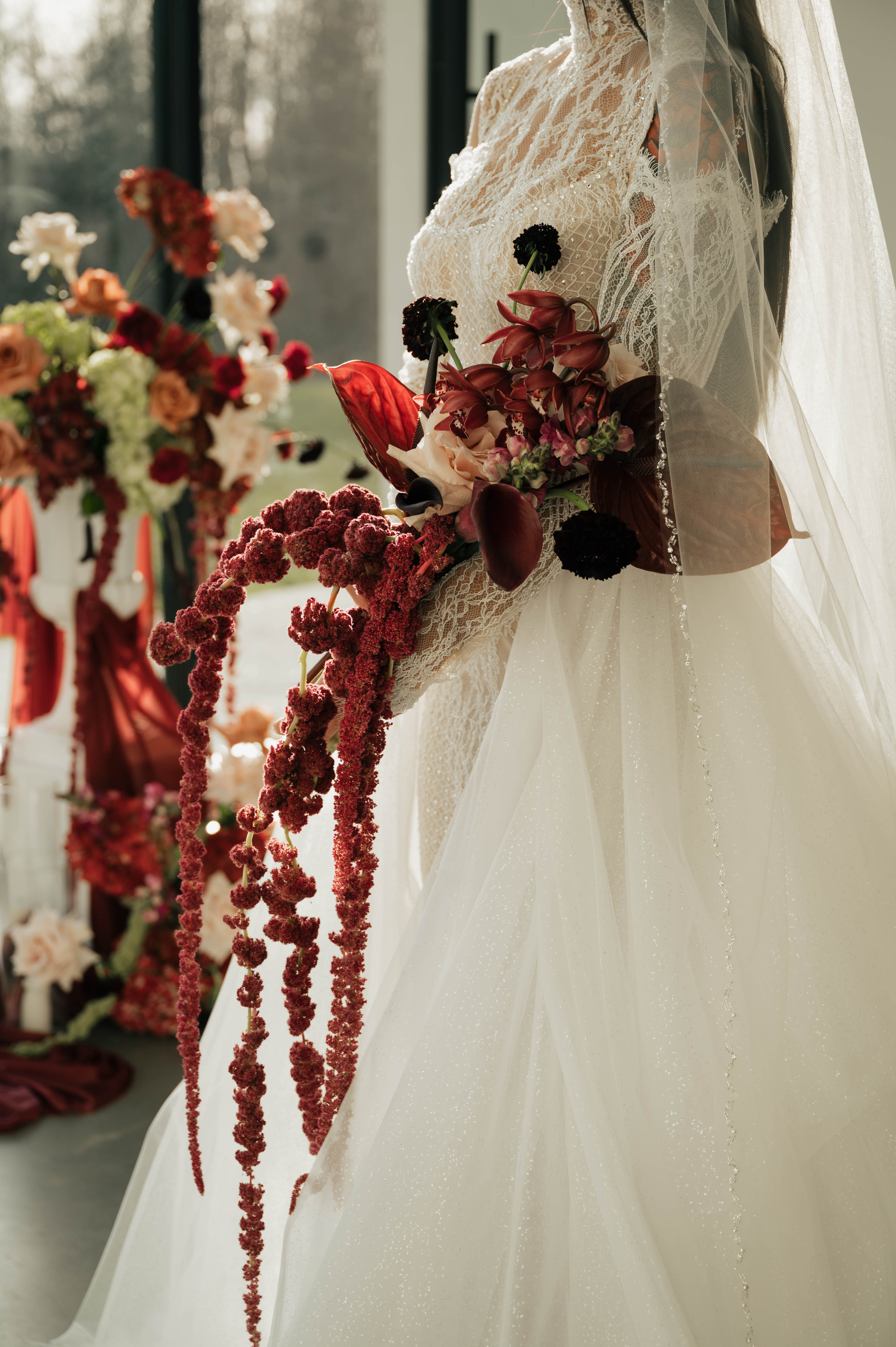Bride in a veil holding an oxblood wedding bouquet with dark burgundy dahlias and trailing amaranthus