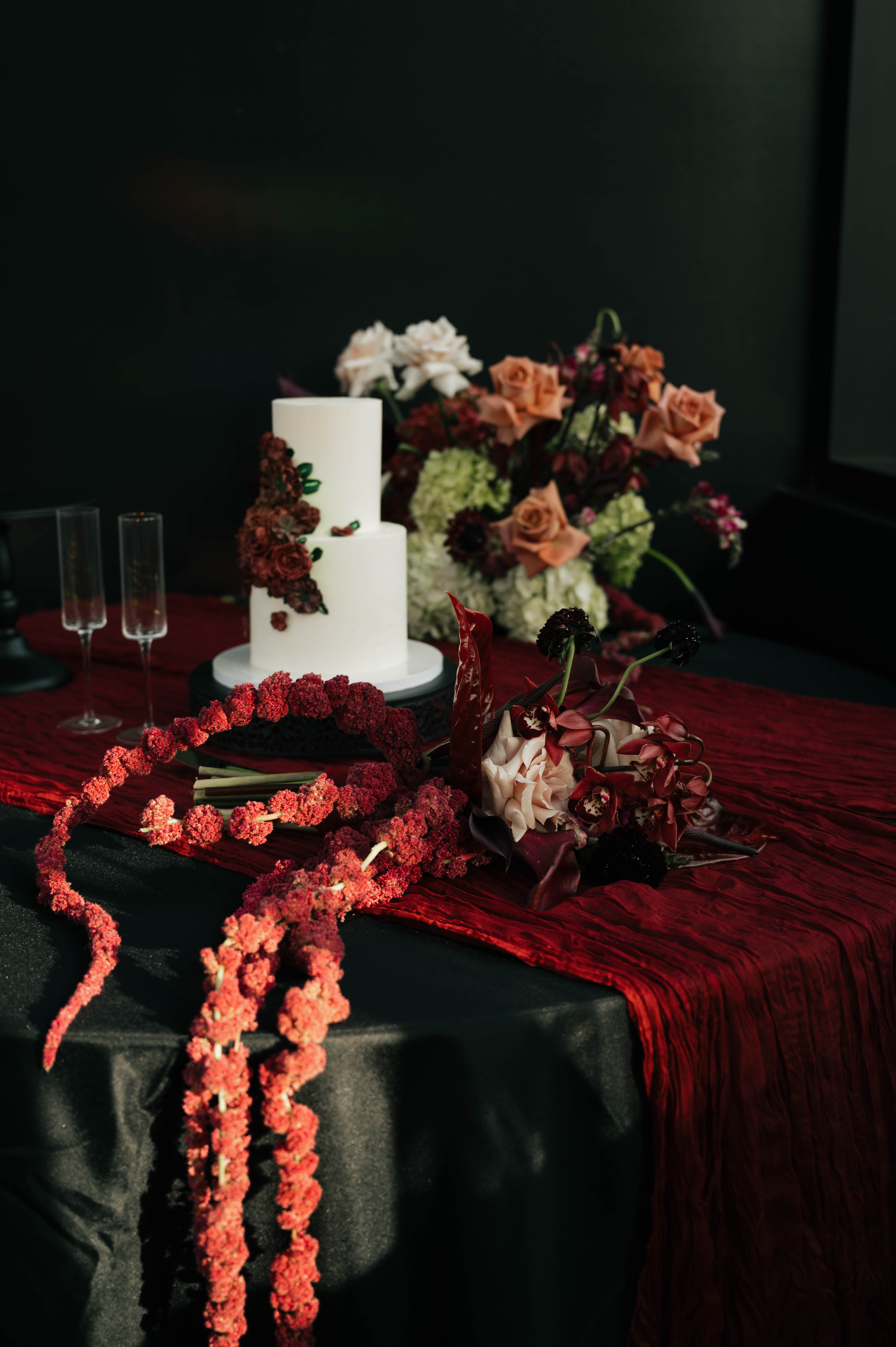 Moody wedding tablescape with burgundy linens, trailing red amaranthus, rust and blush flowers and a white tiered cake