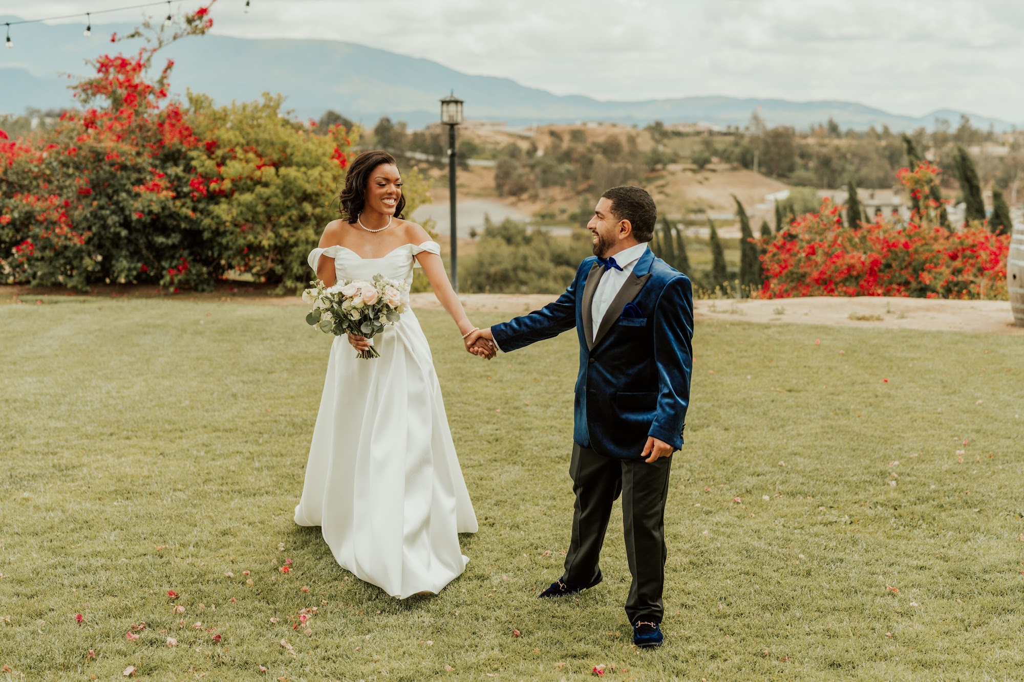 Bride and groom holding hands on the lawn at Callaway Vineyard & Winery with red bougainvillea and the Temecula hills behind them