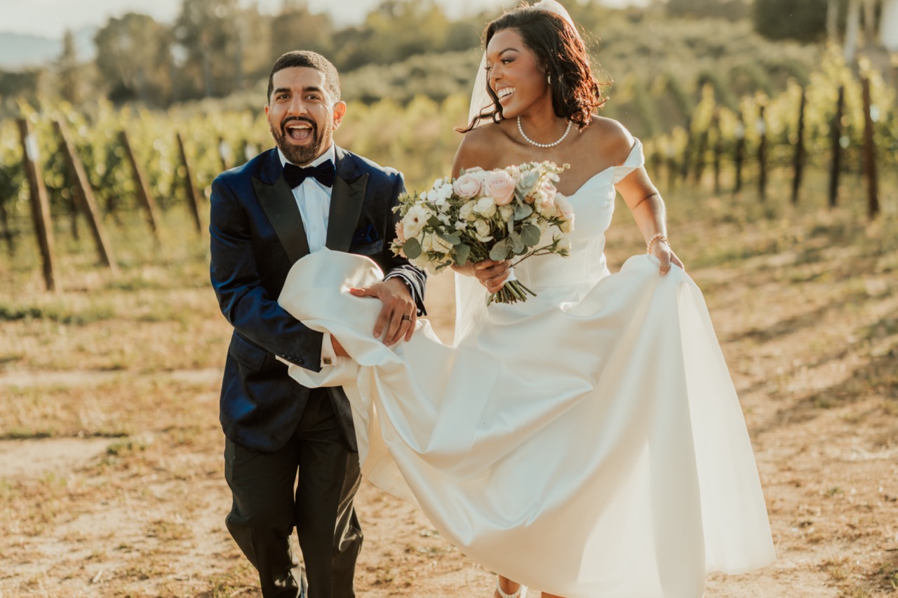 Bride and groom laughing in the vineyard rows at Callaway Vineyard & Winery, bride holding a blush and white rose bridal bouquet