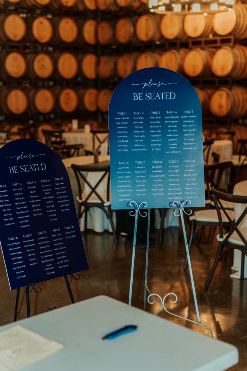 Navy blue seating chart signs in front of stacked oak barrels in the barrel room at Callaway Vineyard & Winery