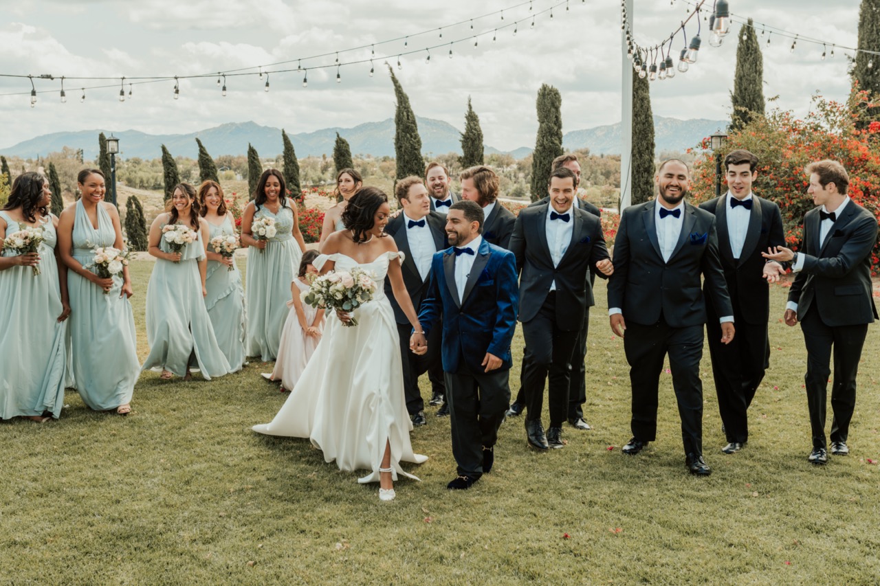Bridal party in sage green dresses carrying blush and white bouquets walking with the couple at Callaway Vineyard & Winery