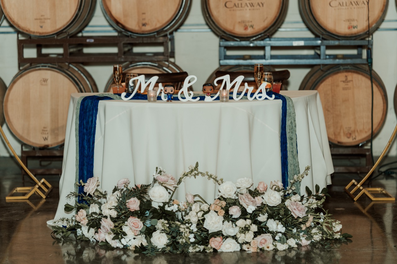 Sweetheart table in the Callaway barrel room with a Mr & Mrs sign and the blush and white ceremony arch flowers repurposed along the front