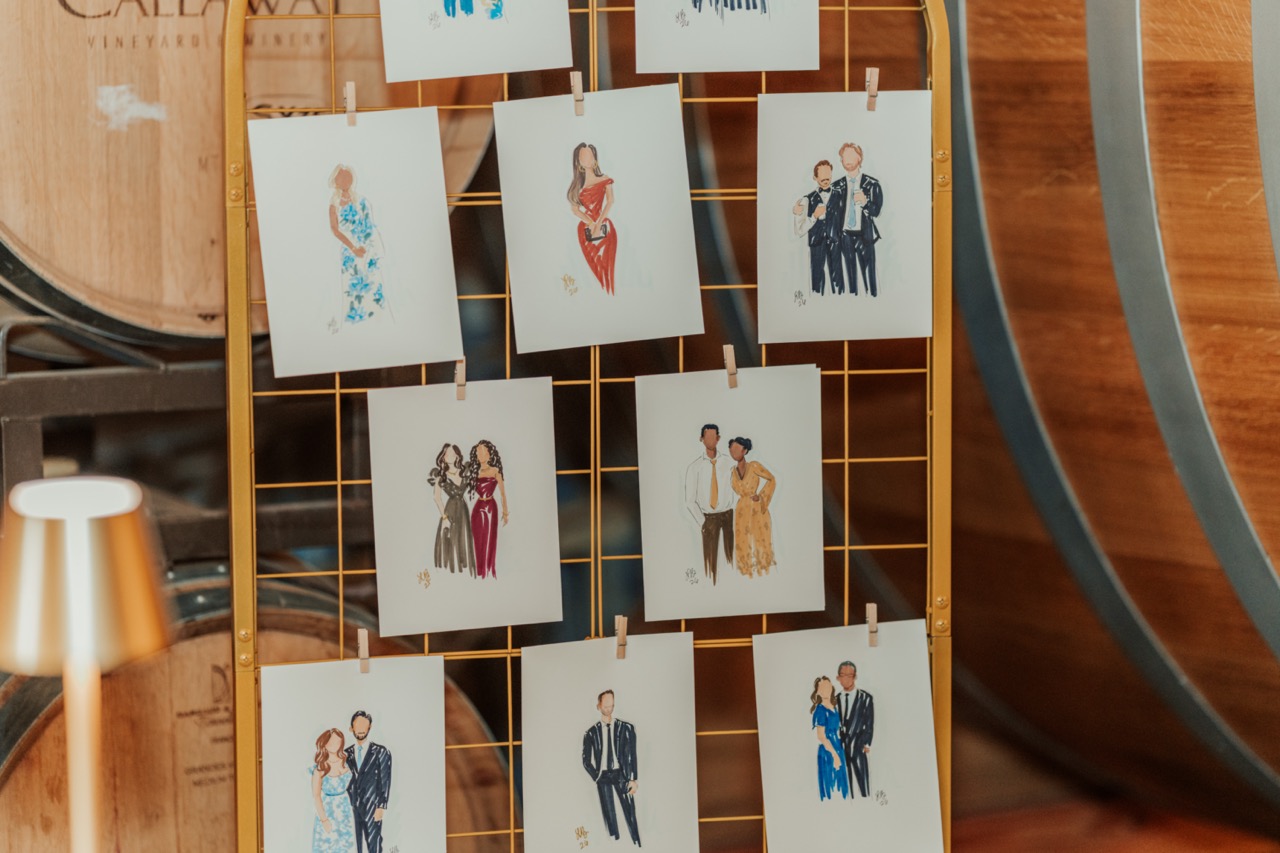 Illustrated guest portraits displayed on a gold grid next to oak wine barrels at Callaway Vineyard & Winery