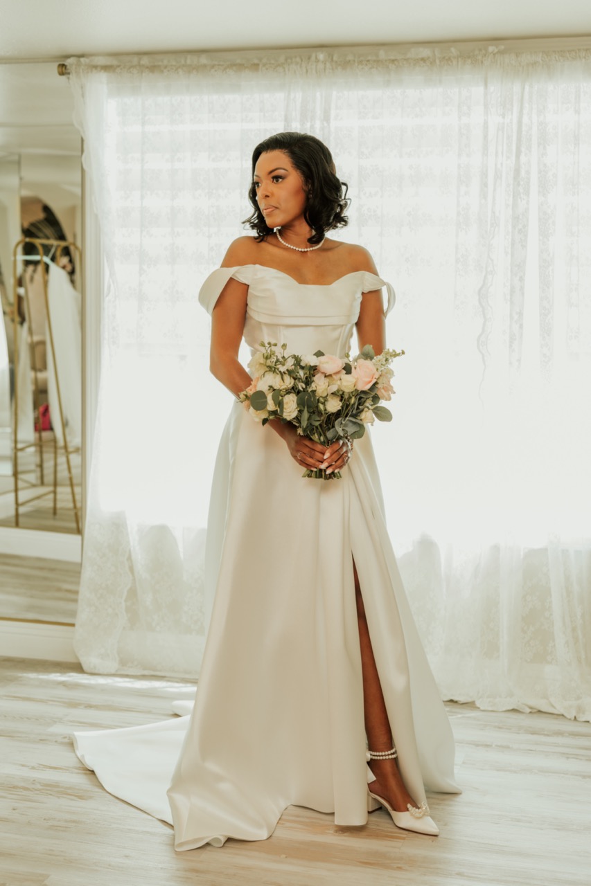Bride in an off-the-shoulder gown holding a blush and white rose bouquet in the bridal suite before the ceremony