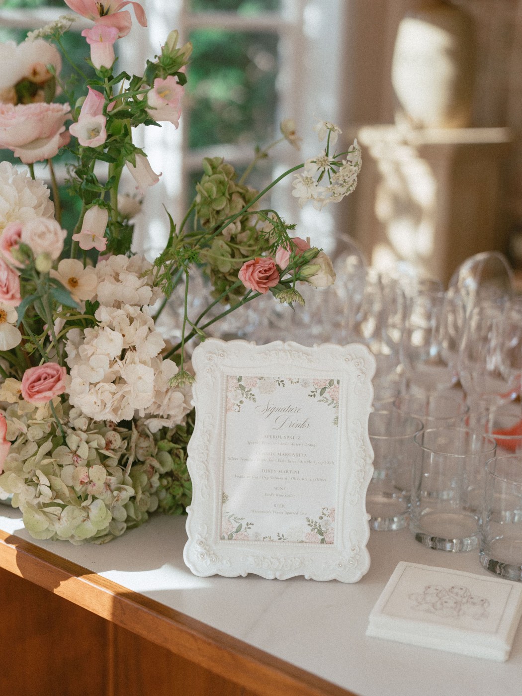 Antique blush and green hydrangea with garden roses and Queen Anne's lace on a wedding bar, next to a framed signature drinks menu
