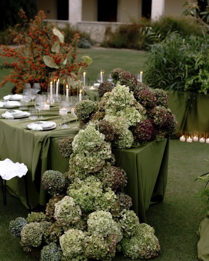 Antique green and burgundy hydrangea spilling from a head table onto the lawn, with olive linens and taper candles for a moody fall wedding