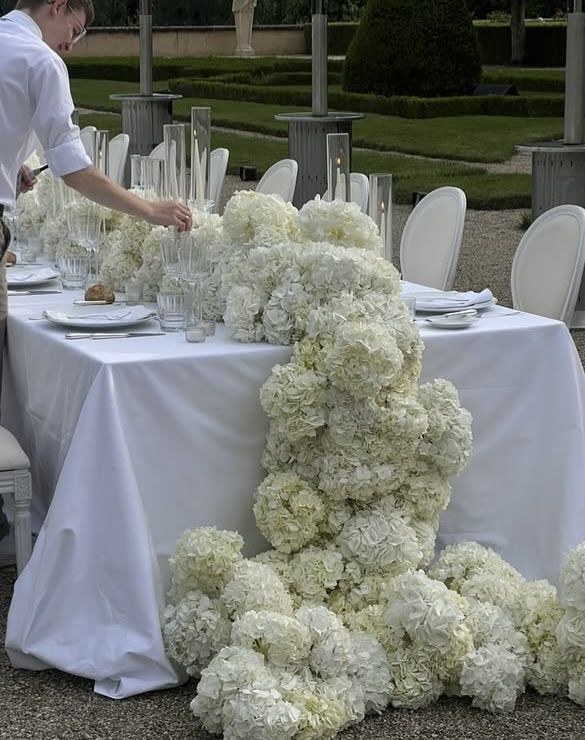 All-white hydrangea cascade running along a long reception table and spilling onto the ground