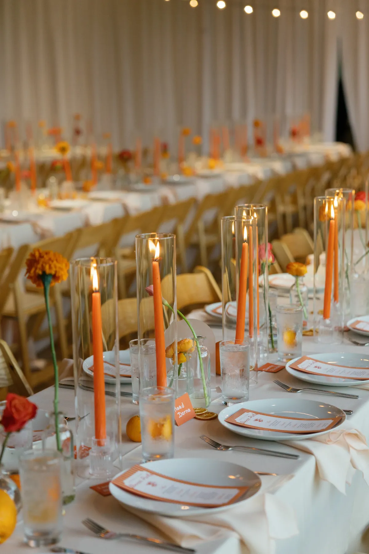 A long reception table set with orange marigolds, roses and tall orange taper candles
