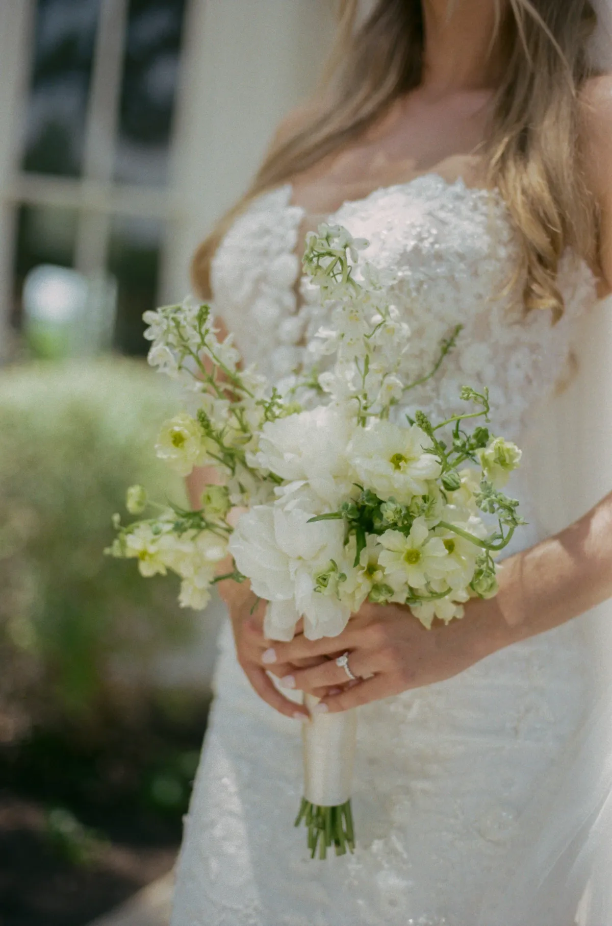 A bride holding a bouquet of white hydrangea, ranunculus and larkspur wrapped in cream ribbon