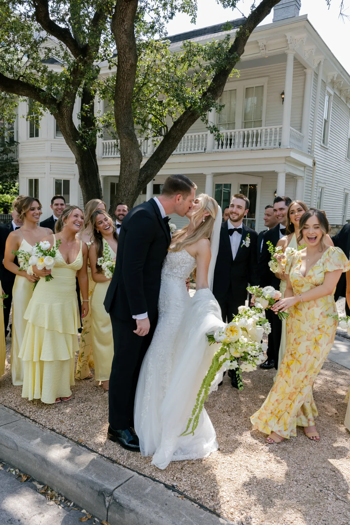 A couple kissing among their wedding party, the bridesmaids holding white and cream bouquets