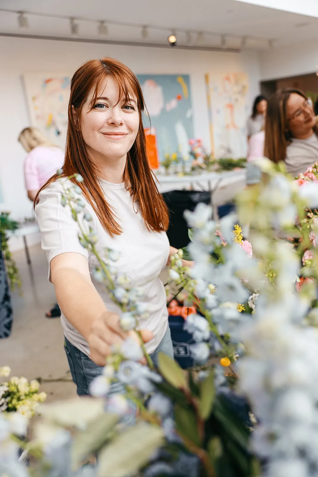 Patrice smiling as she pulls a stem of pale blue delphinium from the buckets