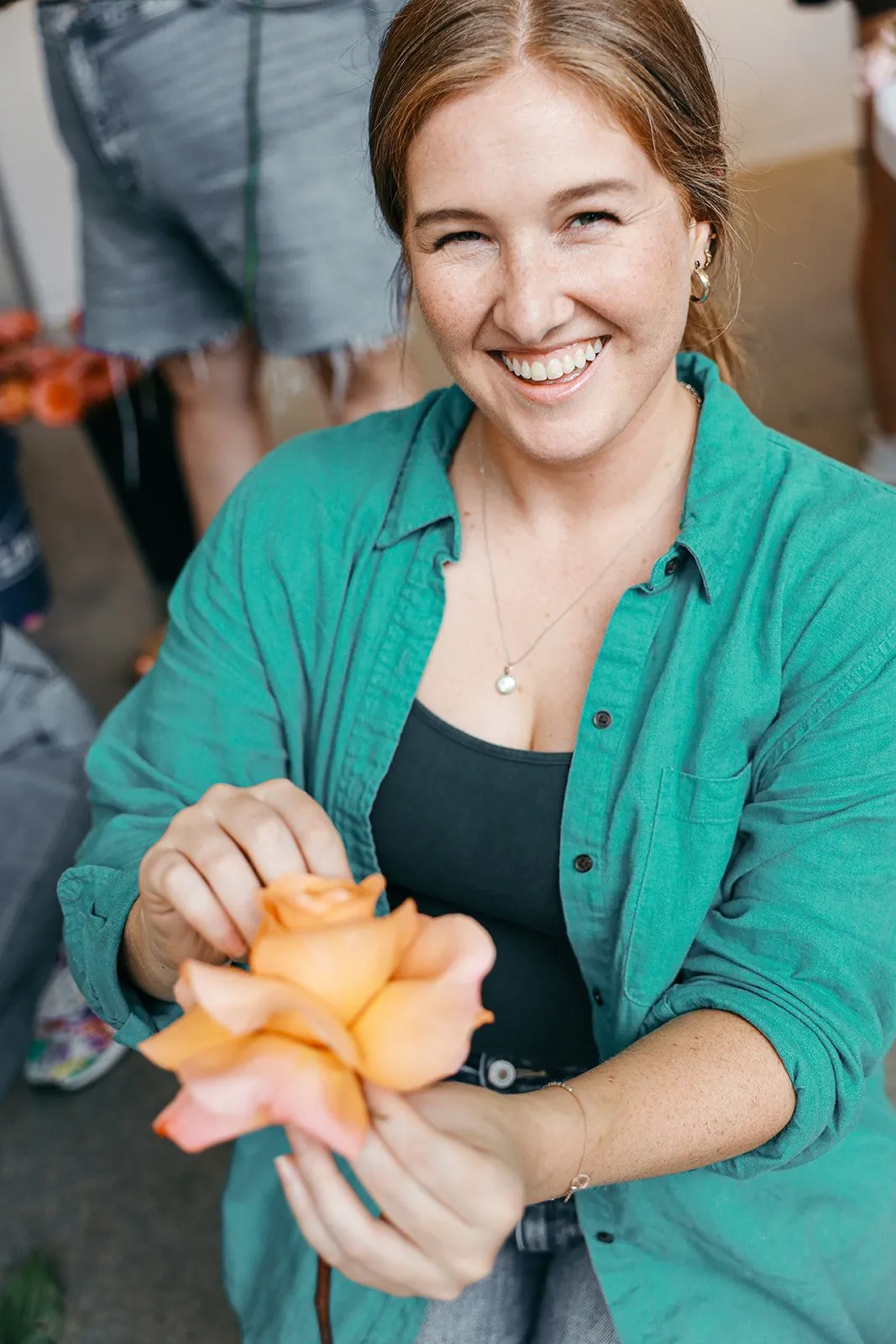 Hannah smiling as she reflexes a peach garden rose, folding back its outer petals to open the bloom