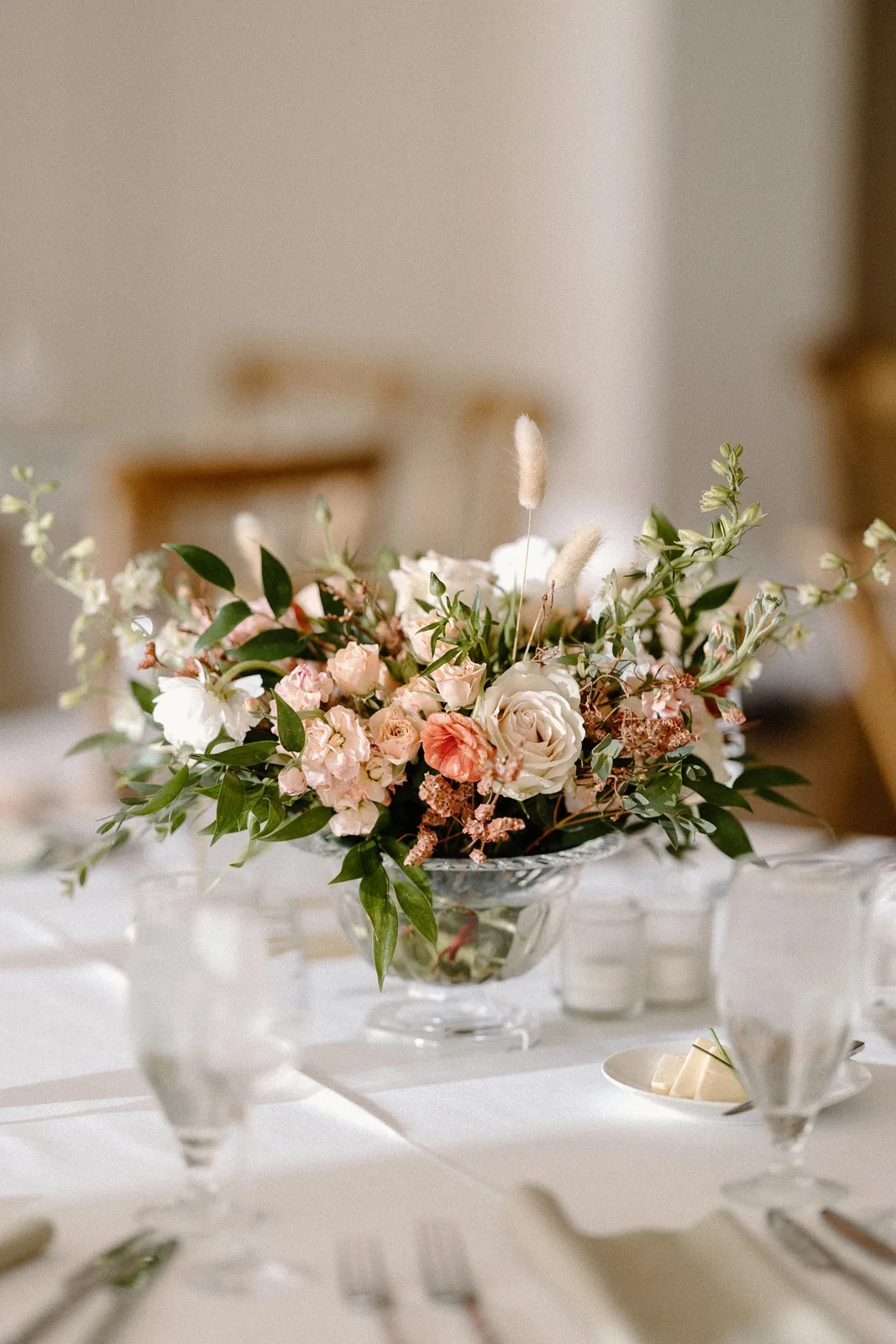 Low garden-style centerpiece of blush roses and spray roses in a clear glass compote on a reception table